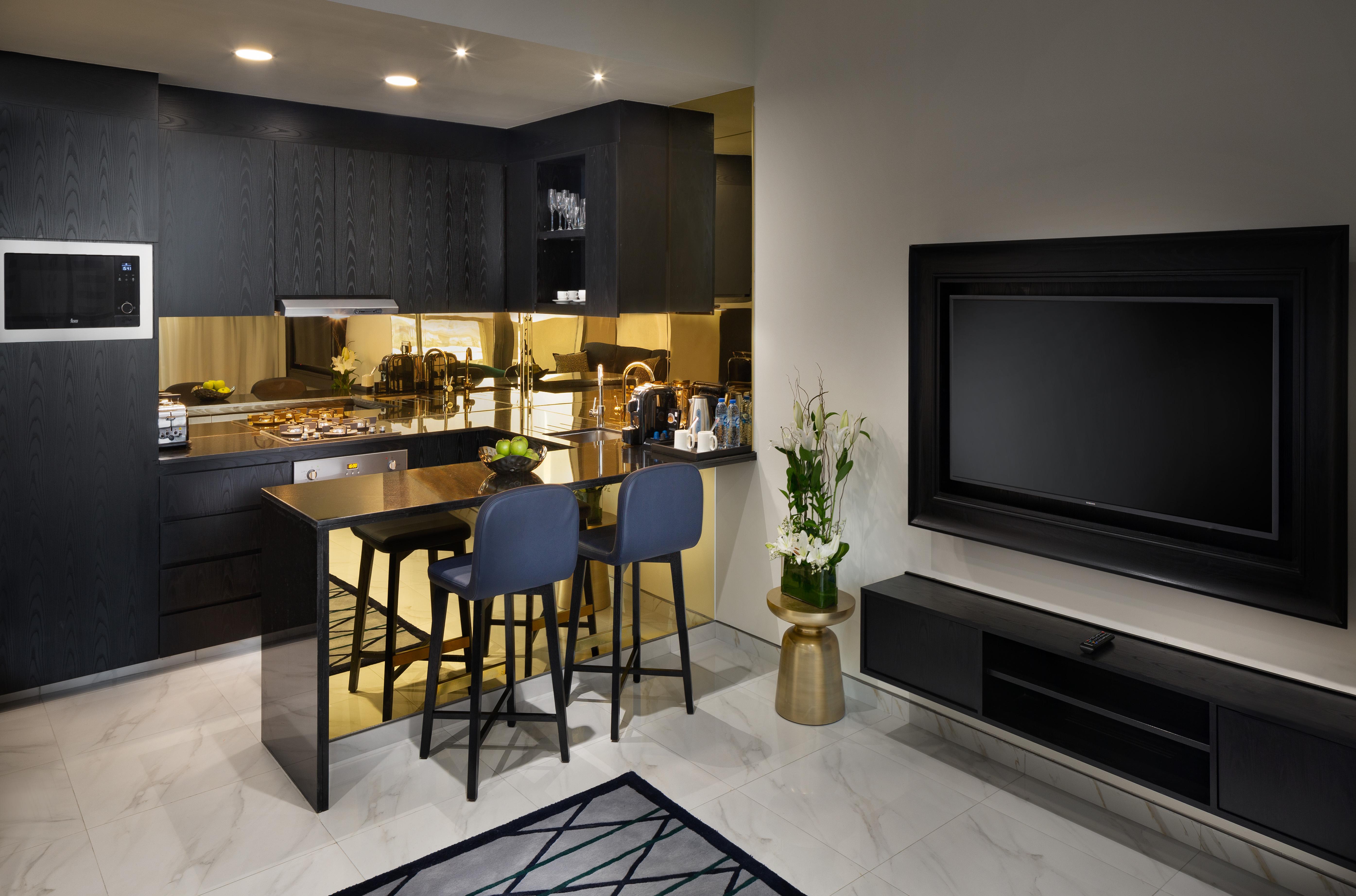 두바이 밀레니엄 아트리아 비즈니스 베이 아파트 호텔 외부 사진 The photo depicts a modern kitchen and living area. The kitchen features dark cabinetry with a clean design, showcasing various appliances, including a stovetop and possibly an oven. There is a kitchen island with two stools, suggesting a space for c