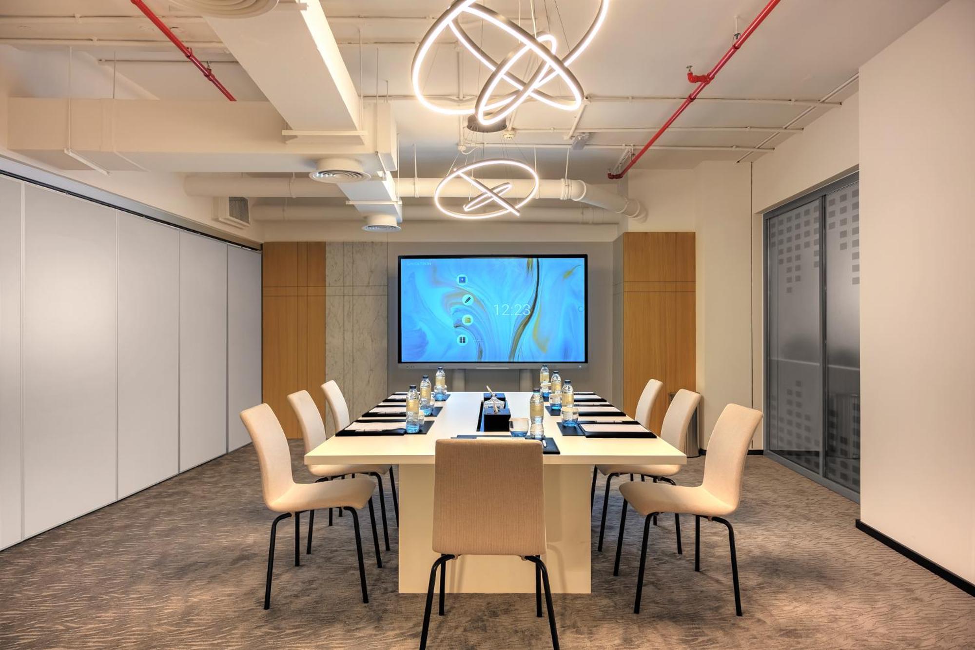 두바이 밀레니엄 아트리아 비즈니스 베이 아파트 호텔 외부 사진 The photo shows a modern conference room designed for meetings. It features a long white table surrounded by beige chairs. At the end of the table, there is a large screen displaying a blue abstract design. The room is well-lit with contemporary ligh