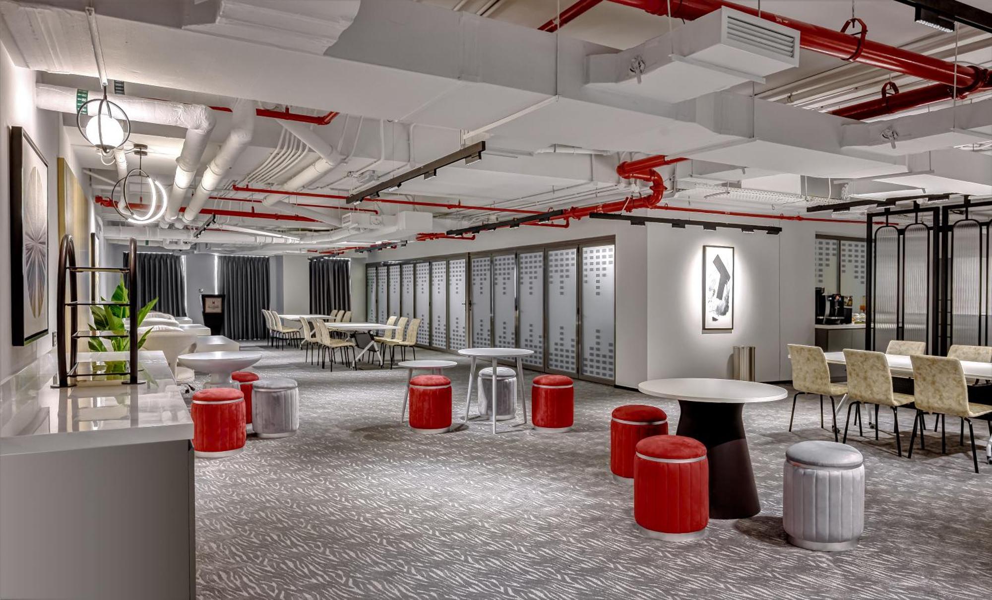 두바이 밀레니엄 아트리아 비즈니스 베이 아파트 호텔 외부 사진 The photo shows a modern interior space, likely an office or communal area. The flooring is covered with a textured carpet, and the ceiling features exposed pipes painted red. 

There are several seating options, including small round tables with sto