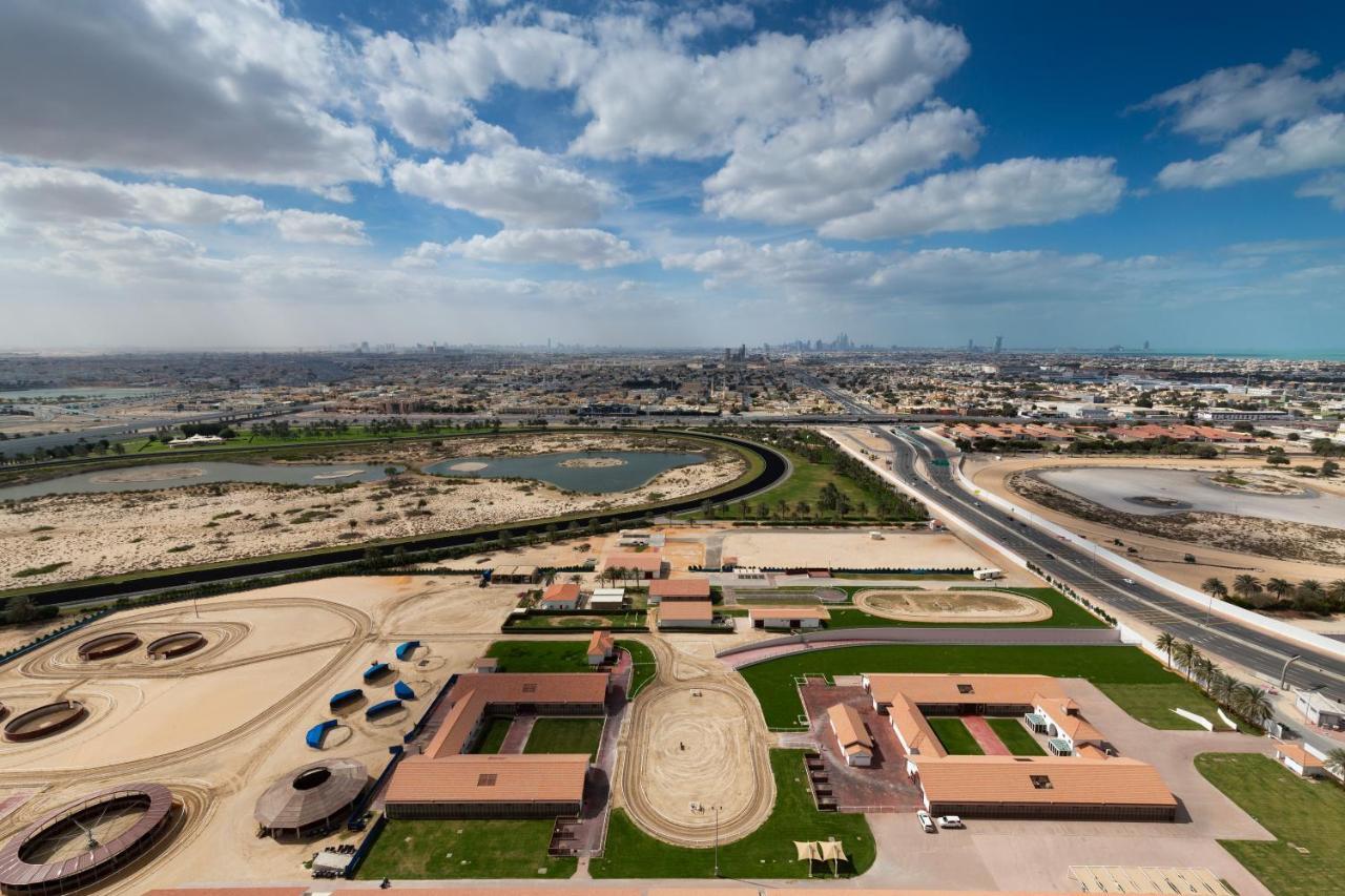 두바이 밀레니엄 아트리아 비즈니스 베이 아파트 호텔 외부 사진 The photo shows a panoramic view of a large landscape with expansive open areas, buildings, and a curved track. In the foreground, there are several stable structures and facilities associated with horse training or racing, surrounded by well-maintai